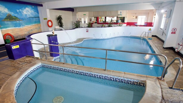 Una piscina interna con due aree distinte, un salvagente e un cartello di avvertimento al muro.