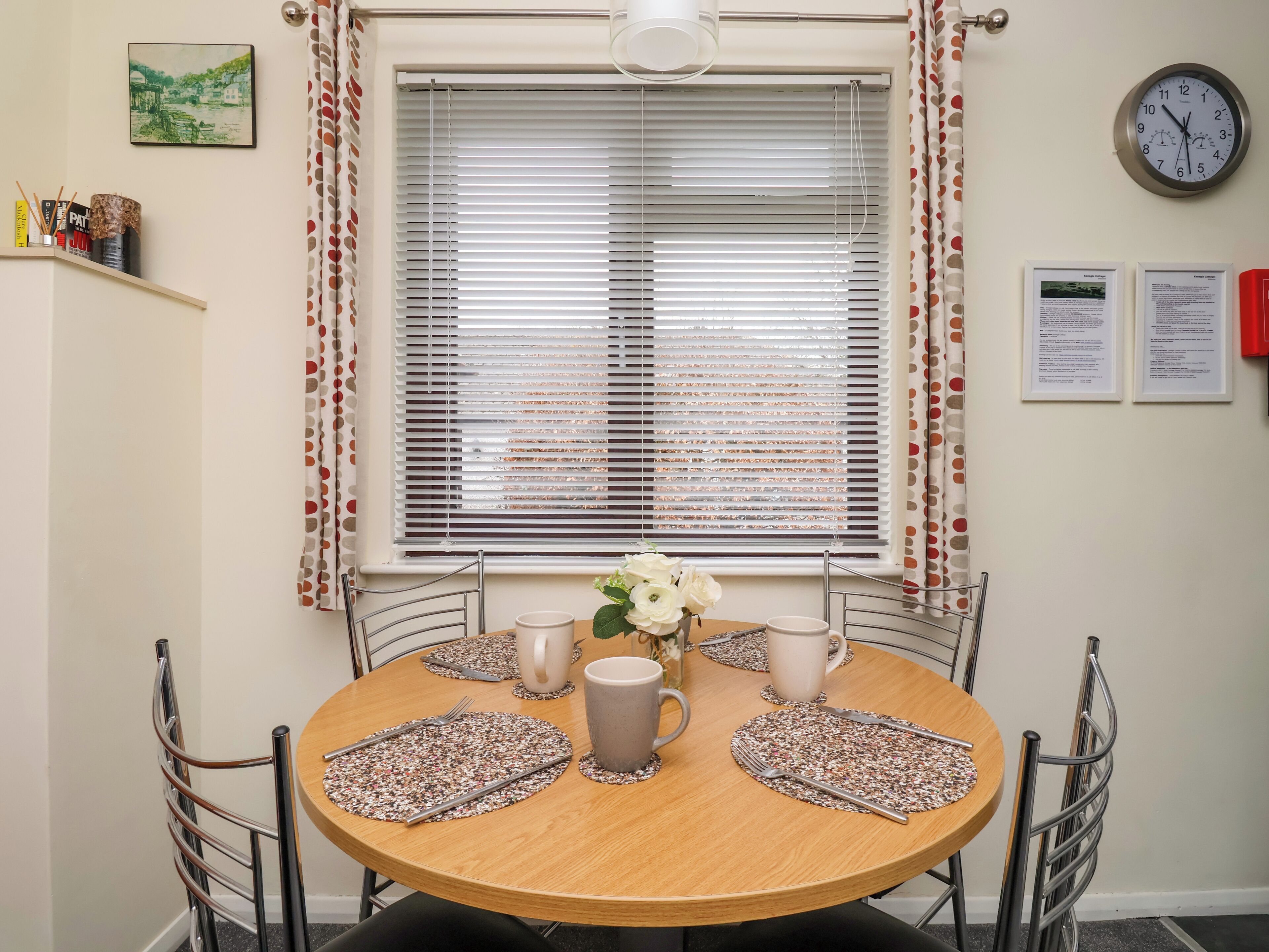 Un comedor con una mesa redonda de madera, cuatro sillas y una ventana con persianas.