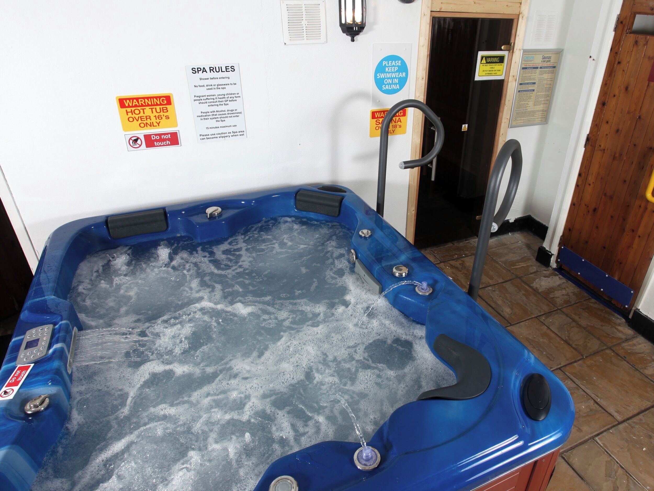 A hot tub with a control panel, surrounded by safety signs and a wooden door.