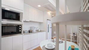 A modern kitchen with built-in appliances, a dining area with a white table, and a small seating area with a white chair. - Extension Berrini (Sao Paulo)