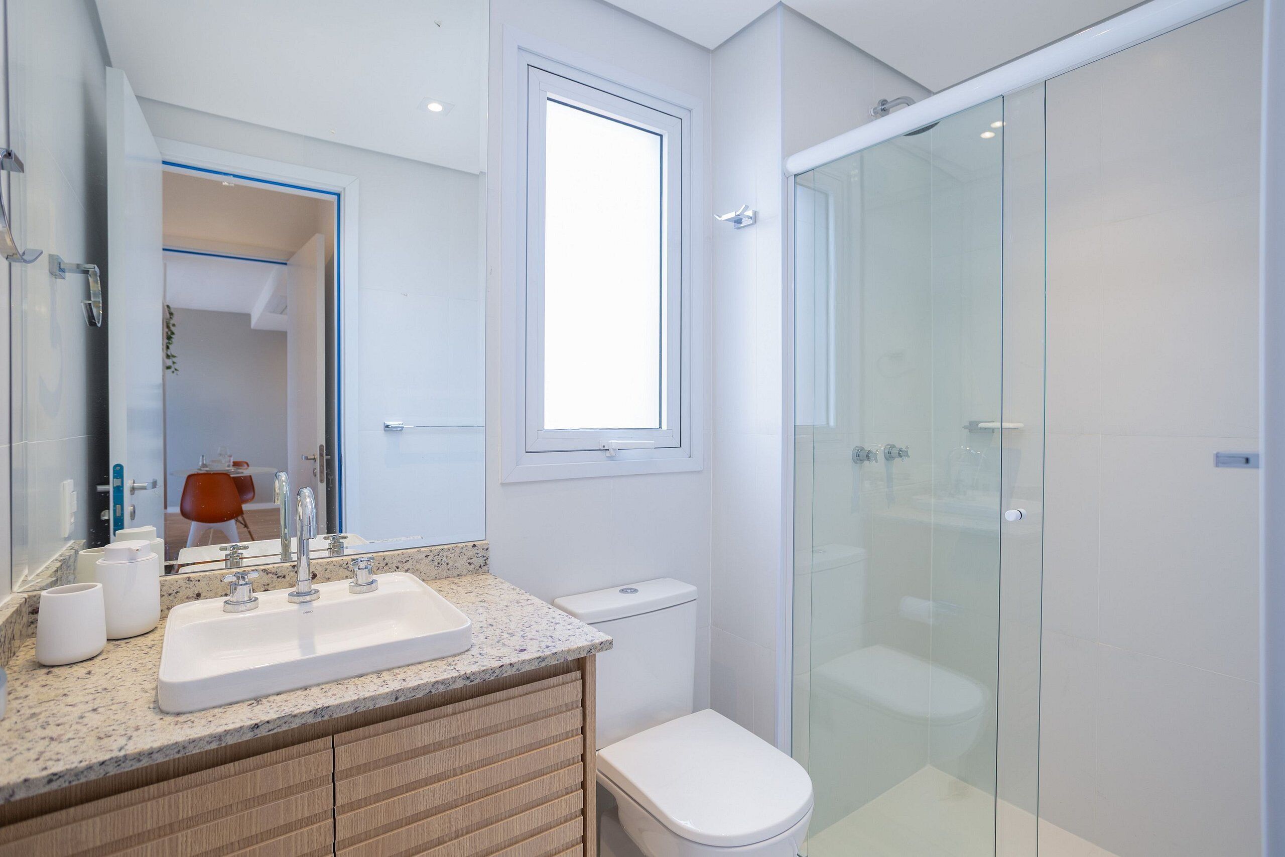 Un baño moderno con cabina de ducha de vidrio, lavamanos blanco sobre encimera de granito y un inodoro.