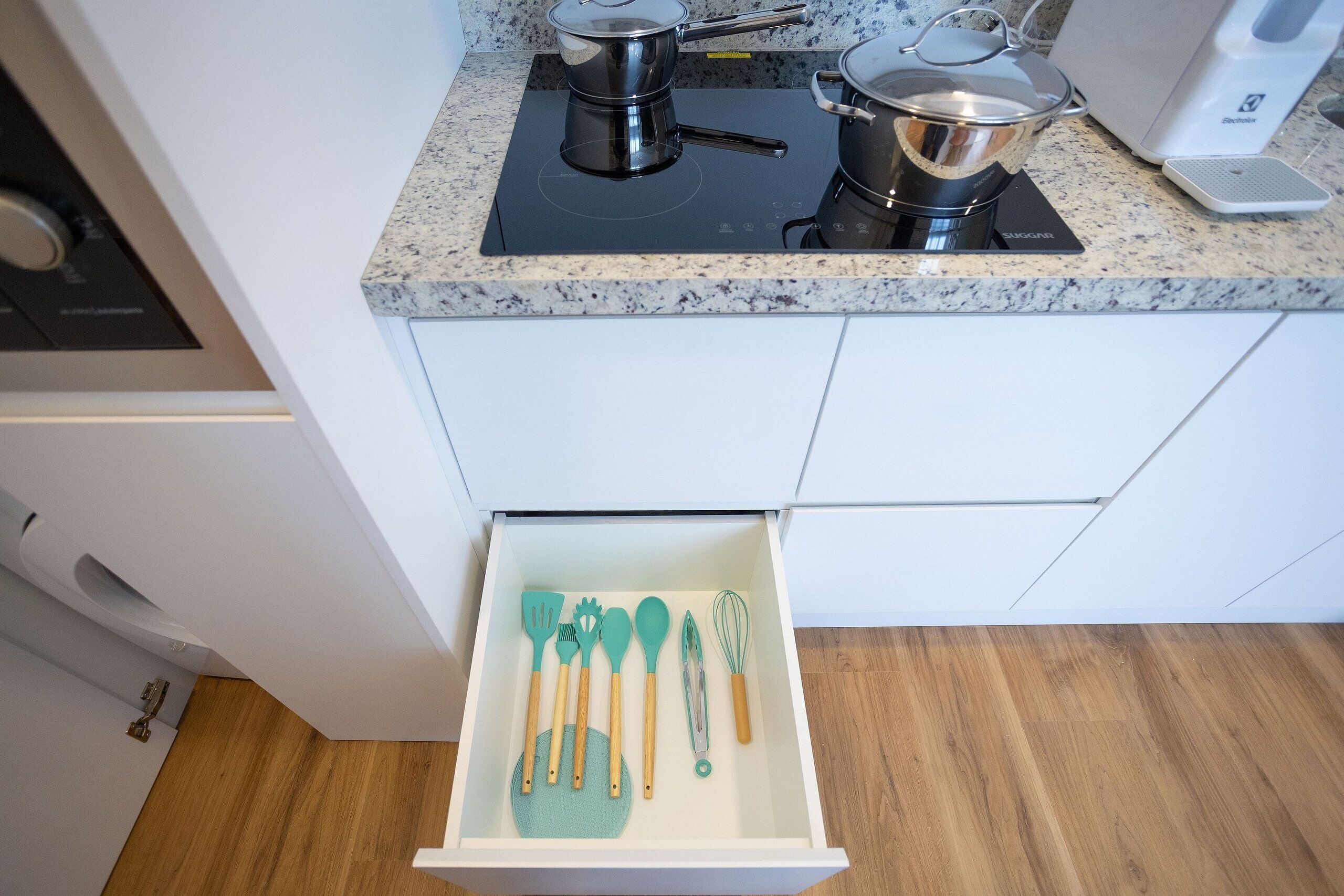 Una cocina con una encimera, estufa y un cajón con utensilios de cocina.