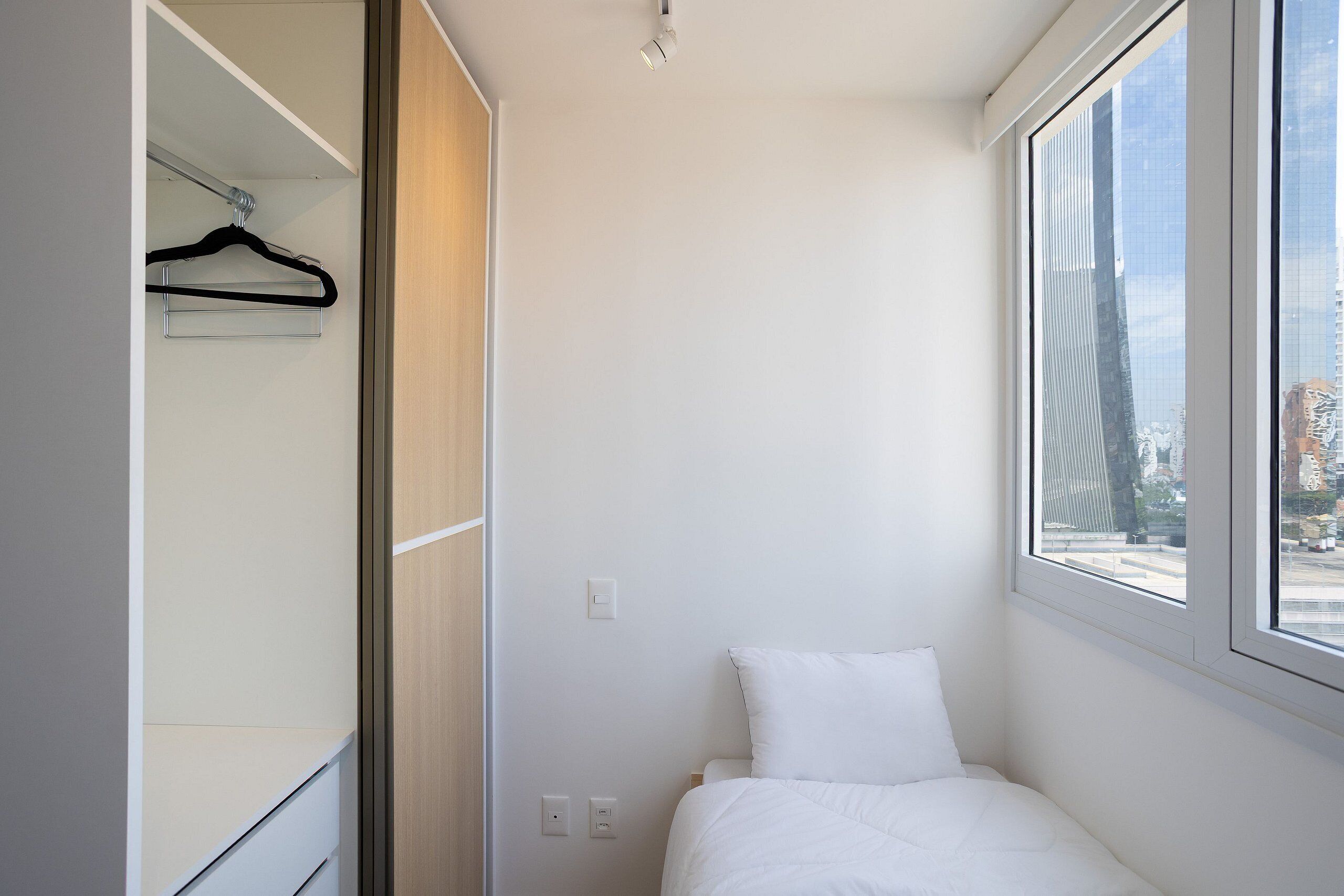 Una habitación pequeña y luminosa con una cama, un ventanal y un armario.