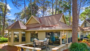 A two-story house with a covered patio, a dining area with chairs and a table, and a small garden area with plants and a bench. - Bay Views ~ Coastal Luxury ~ Golf Cart (Miramar Beach)