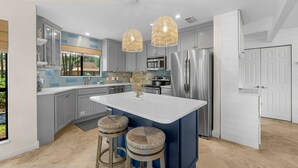 A modern kitchen with grey cabinets, a central island, stainless steel appliances, and two wicker stools. - Bay Views ~ Coastal Luxury ~ Golf Cart (Miramar Beach)