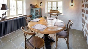 A dining room with a round wooden table, four chairs, a vintage cabinet, and directional signs on the windows.
