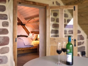 Quarto aconchegante com parede de pedra, vigas de madeira no teto e cama com almofadas florais.