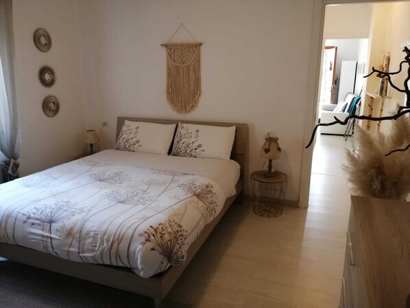 A bedroom with a bed, bedside table, lamp, and decorative wall hanging.