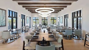 A spacious dining area with a long table and chairs, large windows, and a modern chandelier. - Solara Resort Home with Private Pool Near Disney (Kissimmee)
