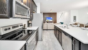 A modern kitchen with a built-in oven, microwave, and dishwasher. A large island with a sink and seating area is in the center. - Solara Resort Home with Private Pool Near Disney (Kissimmee)