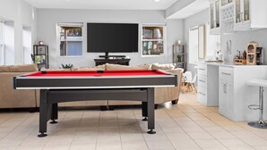Ein modernes Wohnzimmer mit Billardtisch, Flachbildfernseher und Küchenbereich mit weißen Schränken und einem Barhocker.