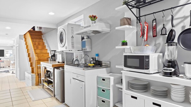 Eine moderne Küche mit weißen Schränken, einem eingebauten Backofen, einer Mikrowelle und einer Kaffeemaschine. Eine Holztreppe führt zu einer weiteren Ebene.