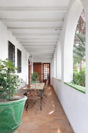 A covered patio with a table and chairs, a potted plant, and a view of the outside.