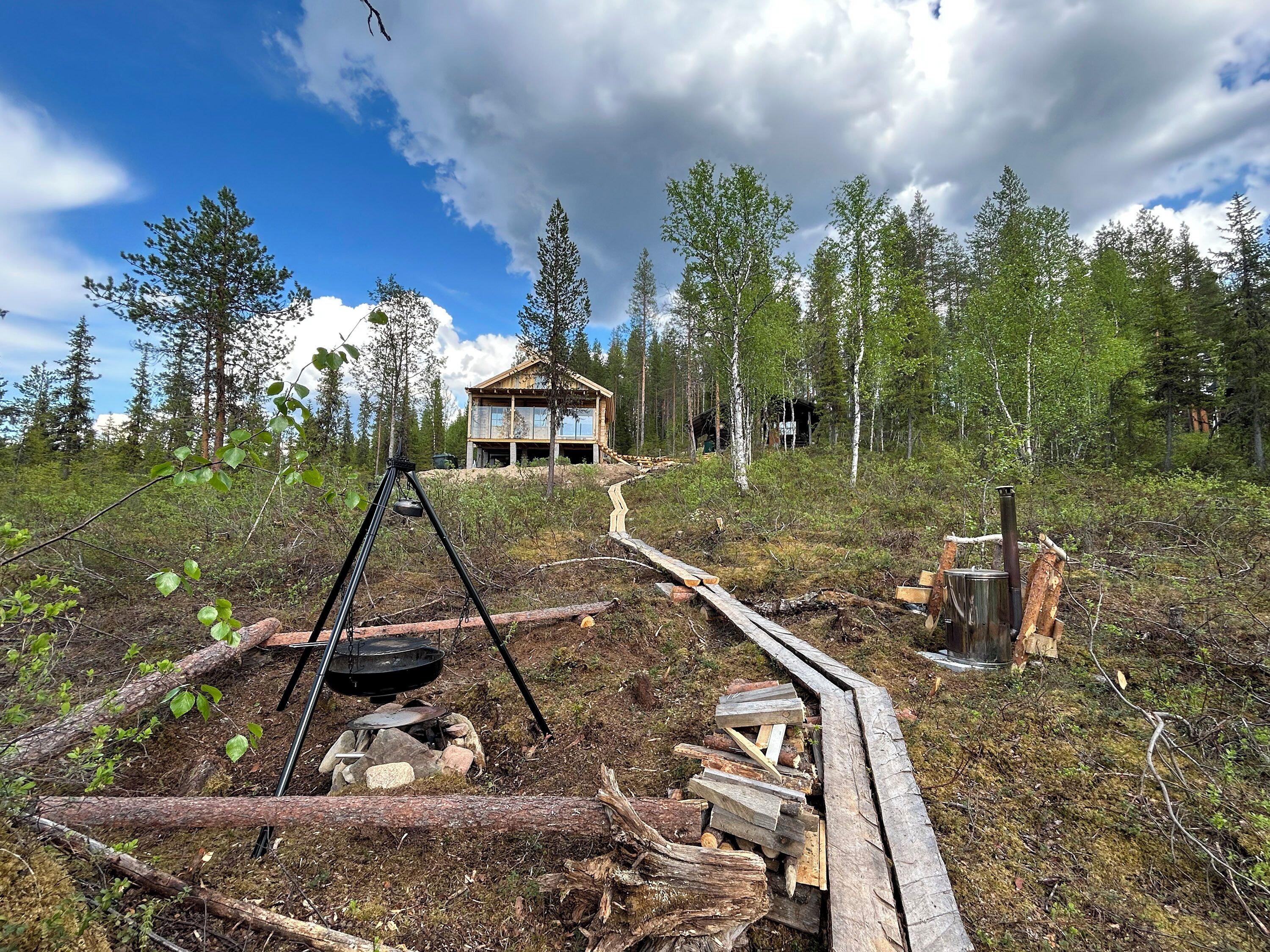 A cabin surrounded by forest, with a swing set and a fire pit in the foreground.