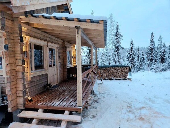 A wooden cabin with a covered porch and a view of snow-covered trees. - Lapland Riverside Nature Cabin (Kolari)