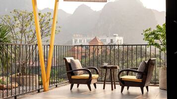 A balcony with two chairs and a small table, overlooking a mountainous landscape.