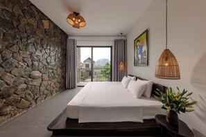 A bedroom with a stone wall, a large bed, a view through a glass door, and a painting on the wall. - Trang An Cozy House (Tay Hoa Lu)