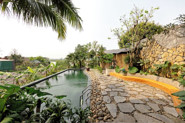 A swimming pool surrounded by stone steps and lush greenery, with a stone wall and a wooden structure in the background. - Trang An Cozy House (Tay Hoa Lu)