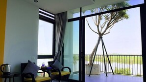Habitación de hotel moderna con un amplio ventanal corredero que da a un balcón con vistas a palmeras y una masa de agua.