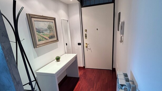 A hallway with a white desk, a framed painting, a door with a handle, and a radiator. - Trilo Rho Fiera Milano House Rino Palmanova 12 (Rho)