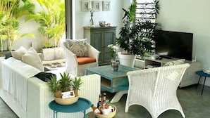 A living room with wicker furniture, a television, and a large window with plants. - Villa Koki Bonheur, house Plain Pied- 700m Plage Pointe aux canonniers (Grand Baie)