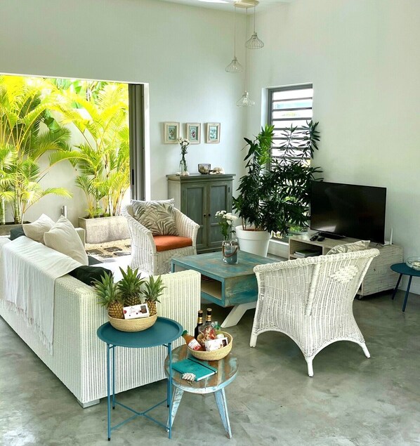 A living room with wicker furniture, a television, and a large window with plants.