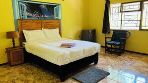 A bedroom with a bed, a nightstand, a chair, a window, and a wall with a tropical mural. - Adrenaline Lodge and Tours (Livingstone)