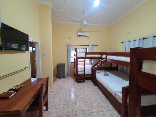 A dormitory room with bunk beds, a desk, a television, and an air conditioning unit.
