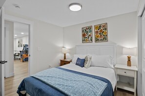 Una camera da letto con un letto, due comodini, una porta che dà su un'altra stanza e due opere d'arte floreali appese al muro.