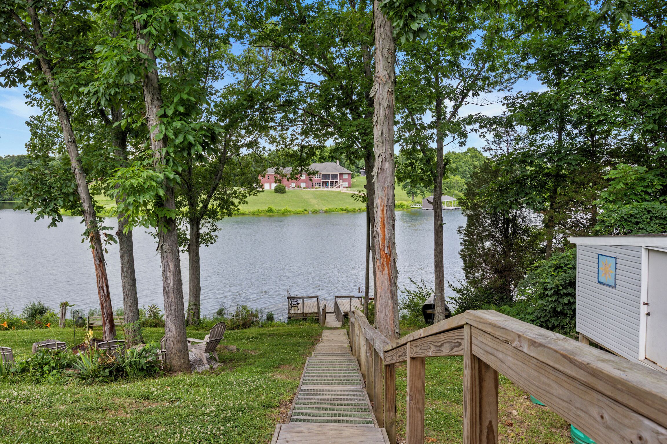 Une terrasse en bois qui mène à un lac, avec une maison en arrière-plan.