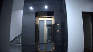 Un ascensor con interior metálico y puerta de vidrio, ubicado entre dos paredes con diseño en blanco y negro.