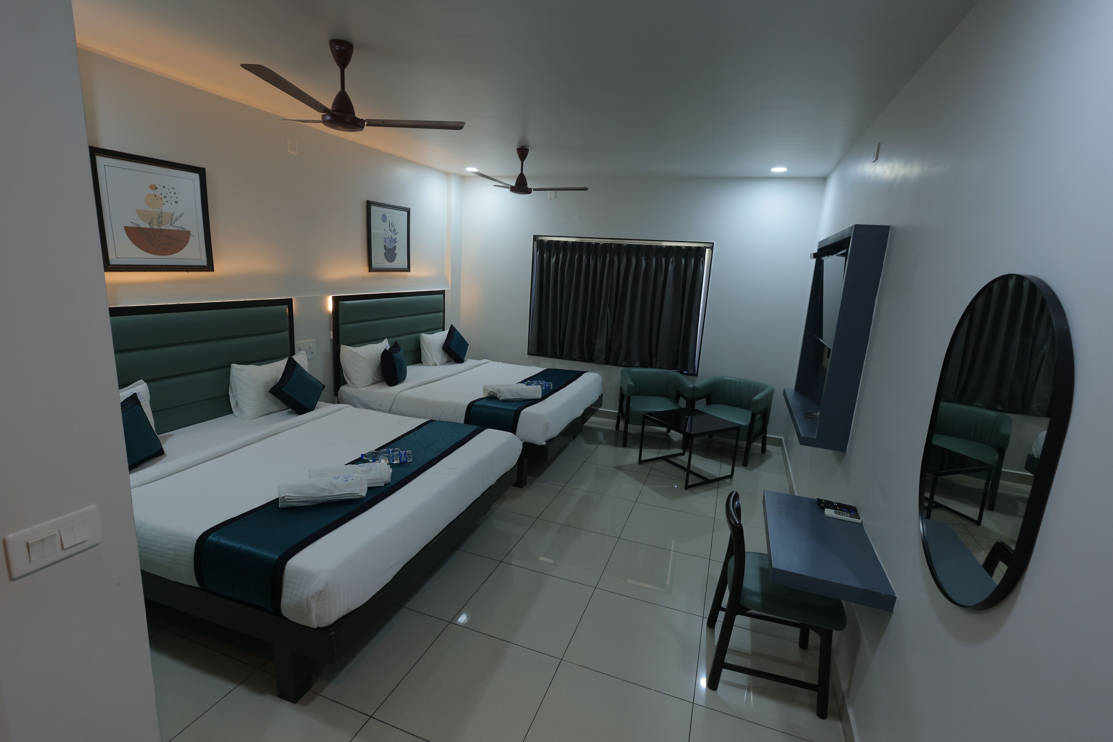 A hotel room with two beds, a desk, a chair, a ceiling fan, and a large mirror.