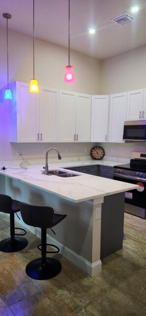 Una cocina moderna con armarios blancos, una isla central con taburetes de bar y luces colgantes.