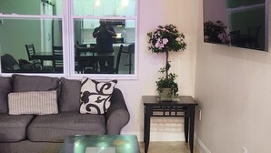 A living room with a sofa, a coffee table, and a TV on a wall. - Modern Place,  3-bedroom house with WiFi, AC, spacious in welcoming Lehigh Acres (Lehigh Acres)