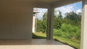 A covered outdoor area with a ceiling fan, surrounded by grass and trees. - Modern Place,  3-bedroom house with WiFi, AC, spacious in welcoming Lehigh Acres (Lehigh Acres)