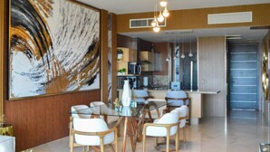 A modern dining area with a glass table, white cushioned chairs, and a large abstract painting on the wall. - Refined Condo w/ Vidanta Access (Nuevo Vallarta)
