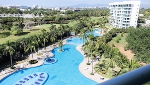 A resort with a large swimming pool, palm trees, and a view of a cityscape in the background. - Refined Condo w/ Vidanta Access (Nuevo Vallarta)