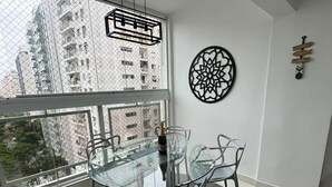 Un espace repas moderne avec une table et des chaises en verre, un élément décoratif mural et une vue sur de hauts immeubles par une grande fenêtre.