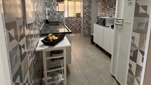 Une cuisine aux murs décorés de motifs, un réfrigérateur blanc et un chariot rempli de fruits.