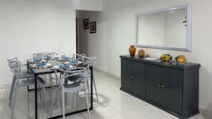 Un coin repas avec une table dressée pour quatre personnes, des chaises blanches, un buffet sombre agrémenté d’objets décoratifs et un ventilateur de plafond.