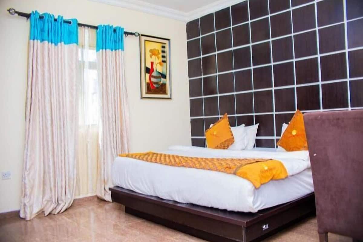 A hotel room with a bed, curtains, a headboard, and a painting on the wall.