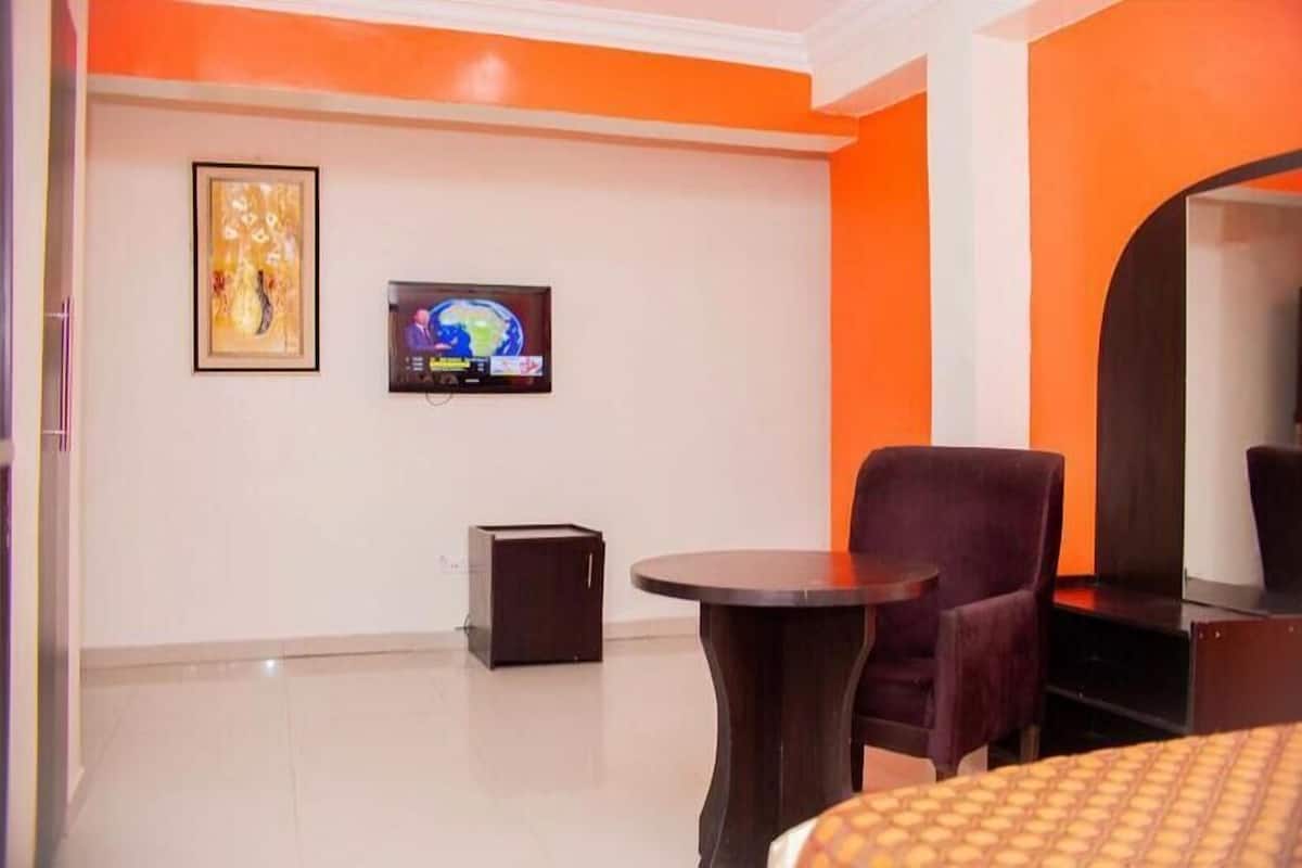 A hotel room with a bed, a small round table, a chair, a TV, and a framed picture on the wall.