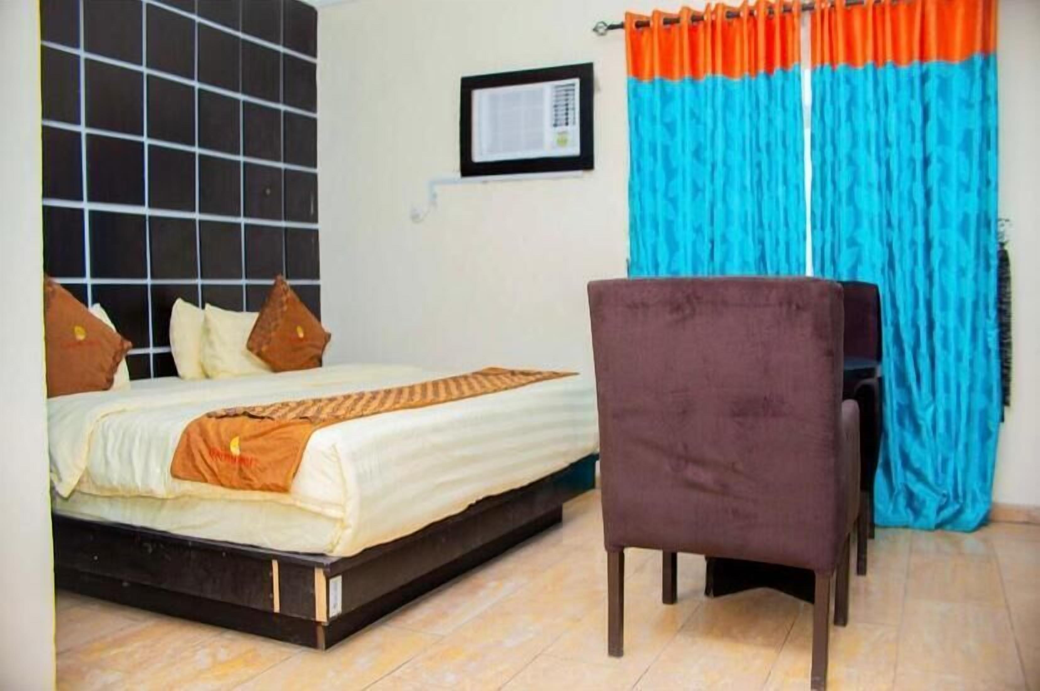 A bedroom with a bed, a chair, curtains, and a wall-mounted air conditioner.