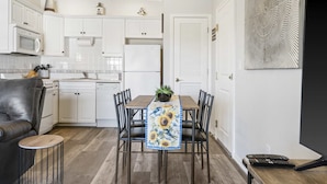 Uma cozinha moderna com armários brancos, uma mesa de jantar com cadeiras, um sofá e uma pequena mesa lateral.