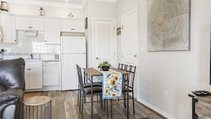 Cozinha moderna com armários brancos, mesa de jantar com cadeiras, mesa de centro e um objeto decorativo na parede.