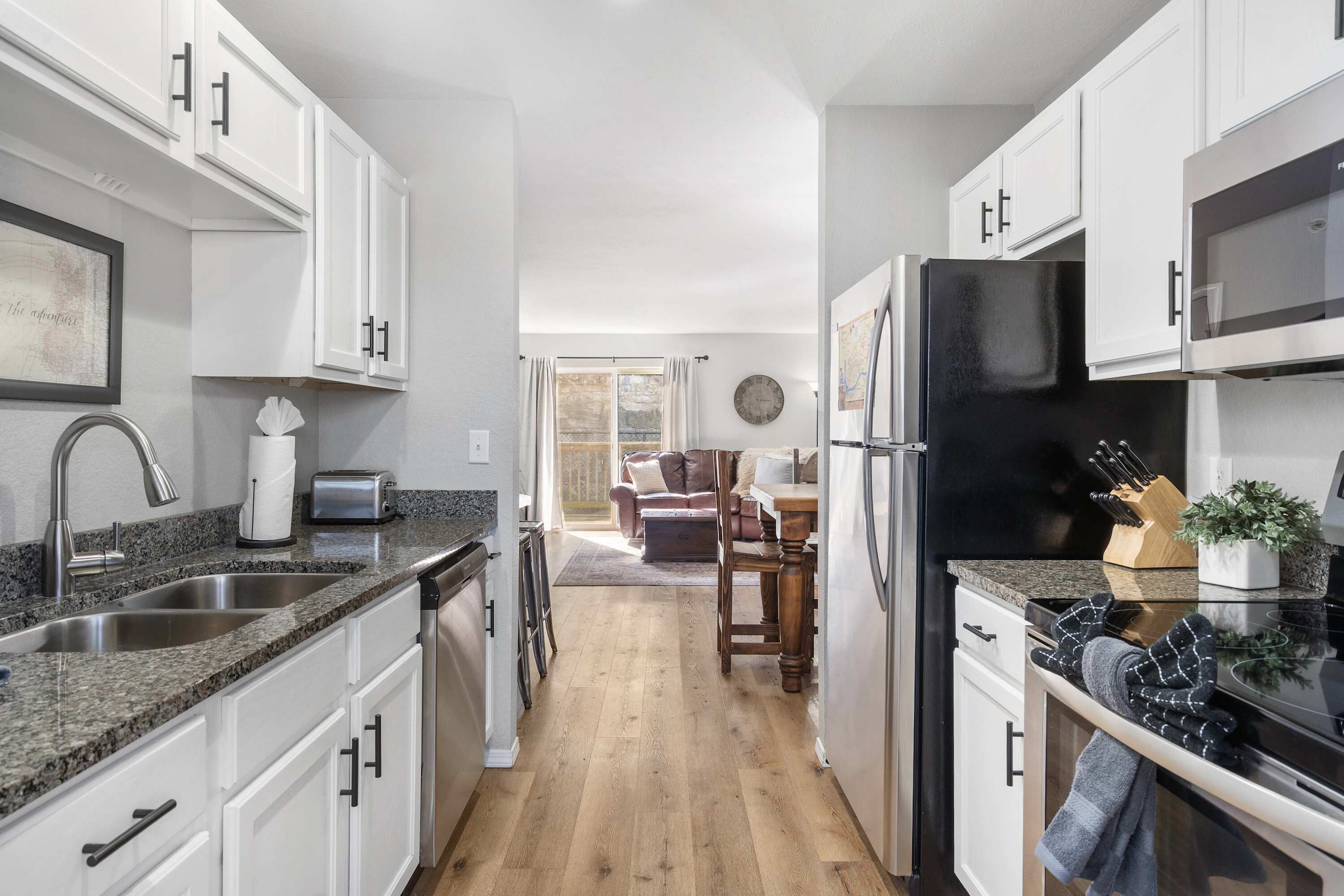 Una cocina moderna con armarios blancos, encimeras de granito, un refrigerador negro y un comedor con mesa y sillas de madera.