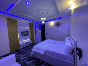 Ein modernes Hotelzimmer mit Bett, einer Sitzecke mit Fernseher und einem Ventilator.
