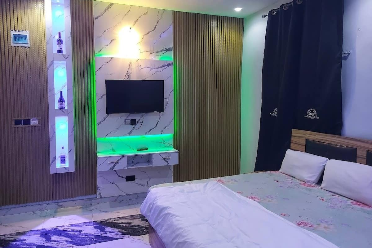 A modern bedroom with a bed, a TV mounted on a marble wall, and a vanity with a green-lit mirror.
