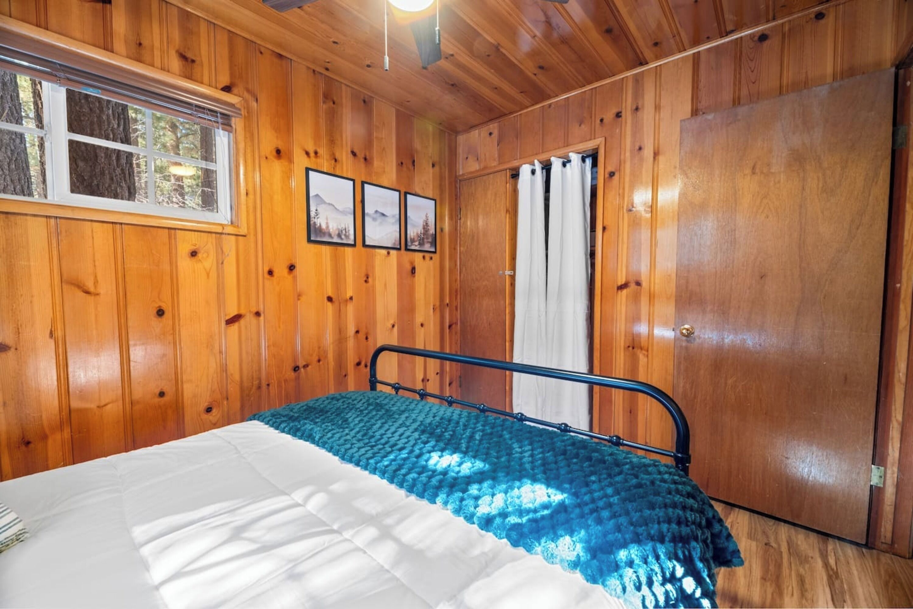 Ein Schlafzimmer mit Holzwänden, einem Bett, einem Fenster und einer Tür.