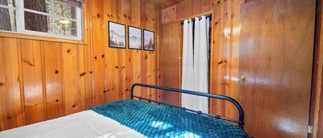 Ein Schlafzimmer mit Holzwänden, einem Bett, einem Fenster und einer Tür.